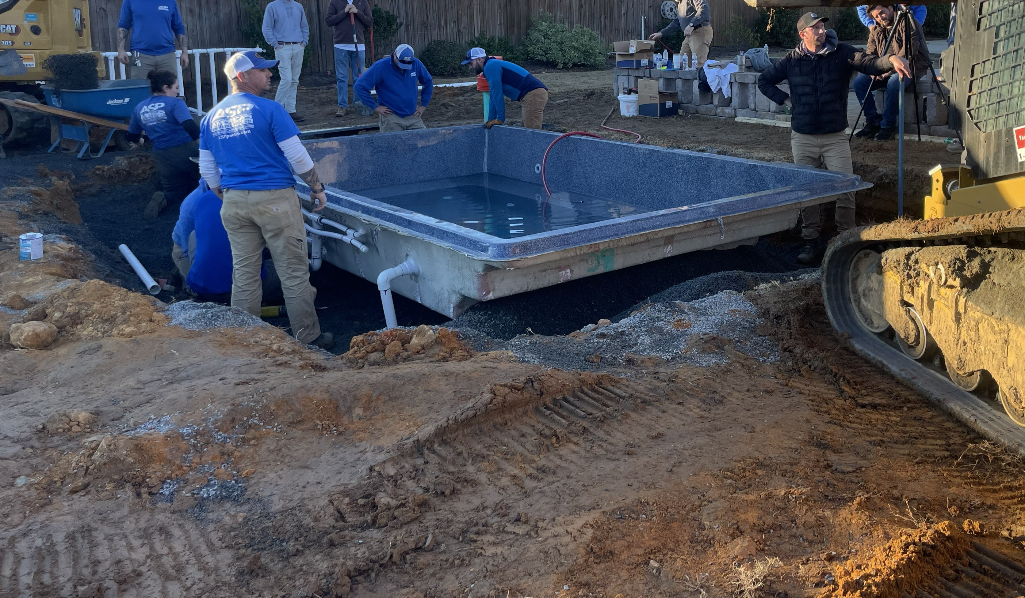 ASP team dropping fiberglass pool shell in backyard