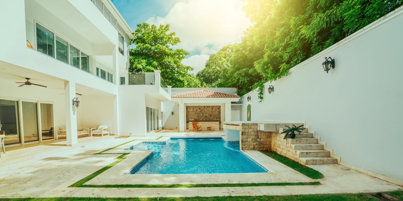A renovated backyard swimming pool with updated tile, coping, waterline, and landscaping in bright daylight.