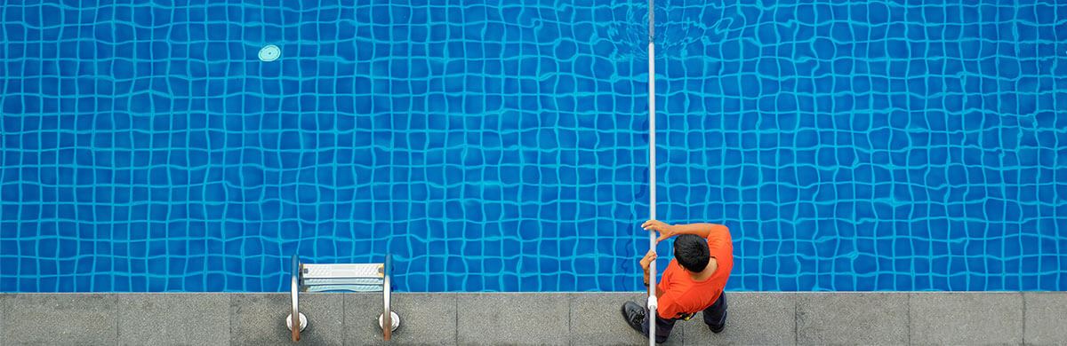 man wearing orange shirt cleaning a swimming pool